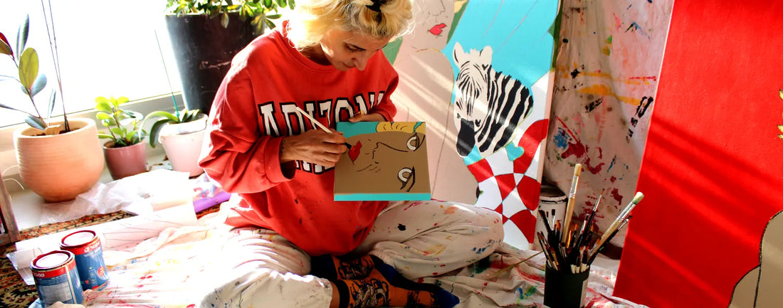 "Liya Ella Raspberry, artist at work in her studio, painting vibrant faces as part of her new creative series. The image captures the authenticity and passion of her process."