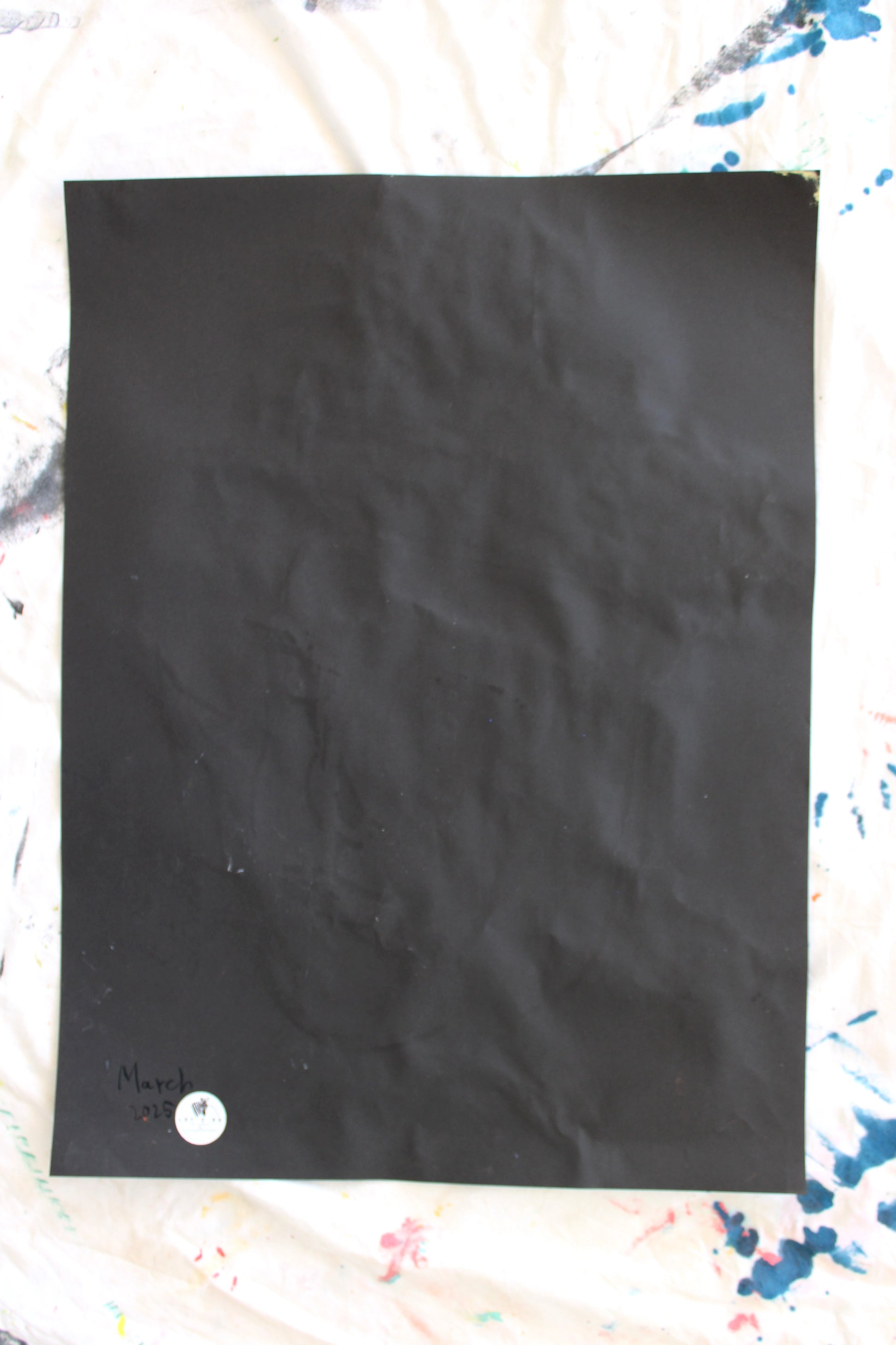 "The back of a black paper with slight creases, featuring the date 'March 2025' written in coal and a 'Let Z Be' logo sticker at the bottom corner, marking the authenticity of the artwork."







