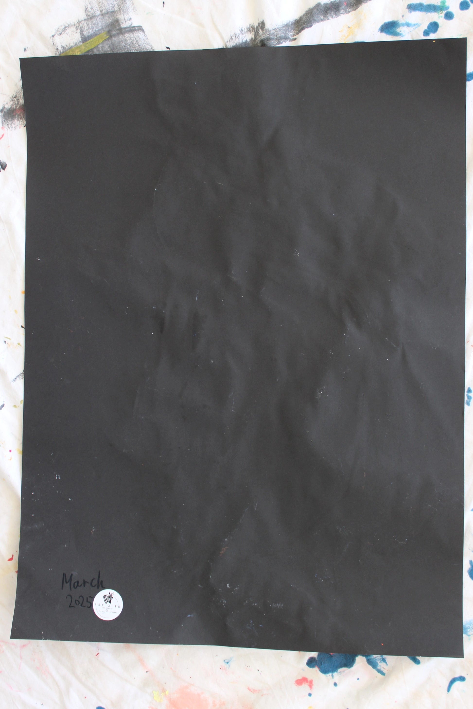 "The back of a black paper with slight creases, featuring the date 'March 2025' written in ink and a 'Let Z Be' logo sticker at the bottom corner, marking the authenticity of the artwork."

