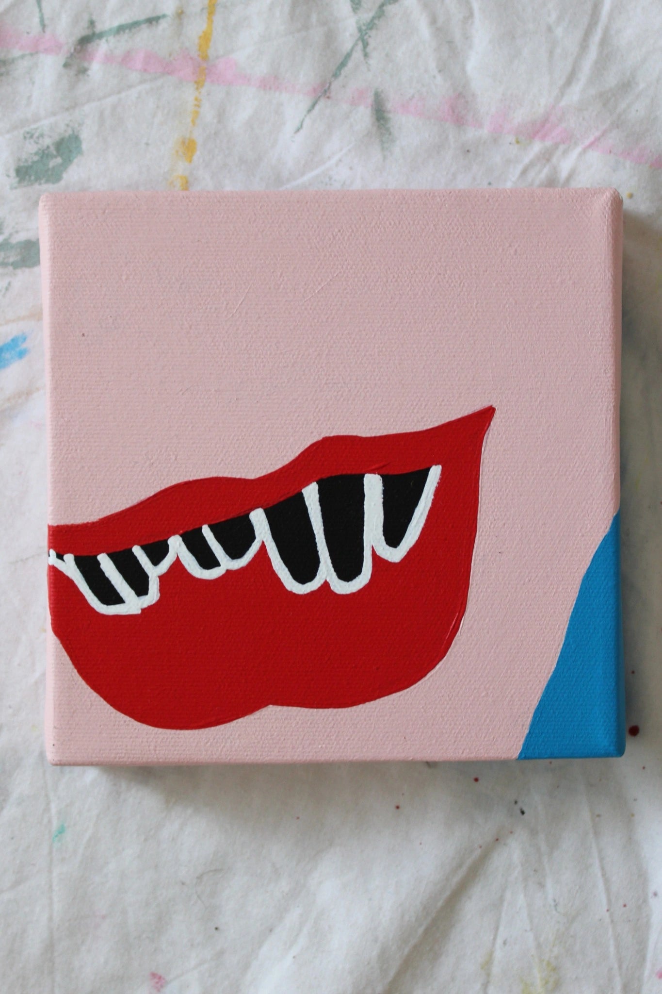 "Minimalist pop art painting of a bold red mouth with sharp white fangs on light pink skin and blue corner background, from the PLAY ME. BOY. art series by Liya Ella Raspberry exploring the physical body and gaze in contemporary art."