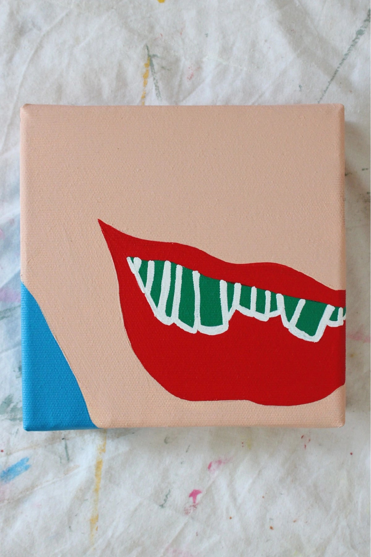 "Contemporary acrylic painting of red lips with green and white striped teeth on a peach-toned face and vibrant blue edge — part of the 'PLAY ME, BOY.' art series by Liya Ella Raspberry, June 2025."