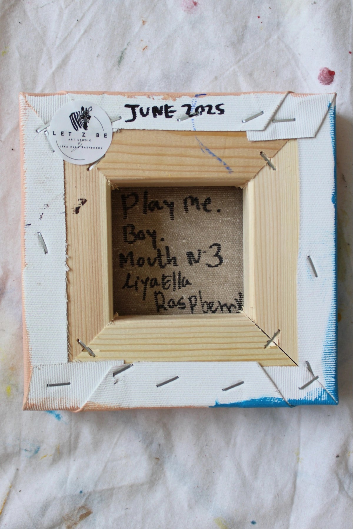 Backside of original canvas painting signed “Play Me. Boy. Mouth N°3” by Liya Ella Raspberry. Let Z Be logo sticker and date marked June 2025 visible on stretcher bars.